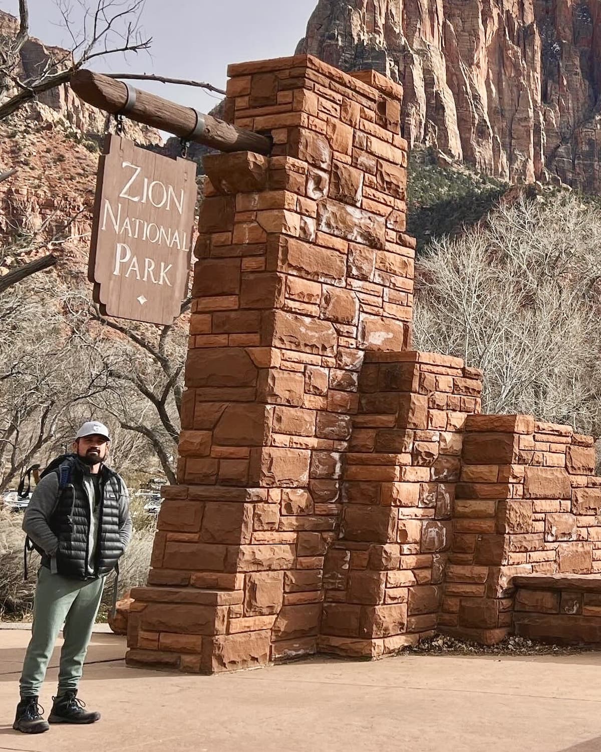 Kyle, founder of The Park Concierge, standing beside the Zion National Park entrance sign with red canyon walls behind him